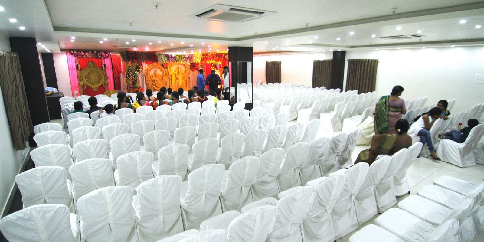 Swathi Hall with chairs neatly arranged and a decorated pulpit in front at Hotel Green Apple