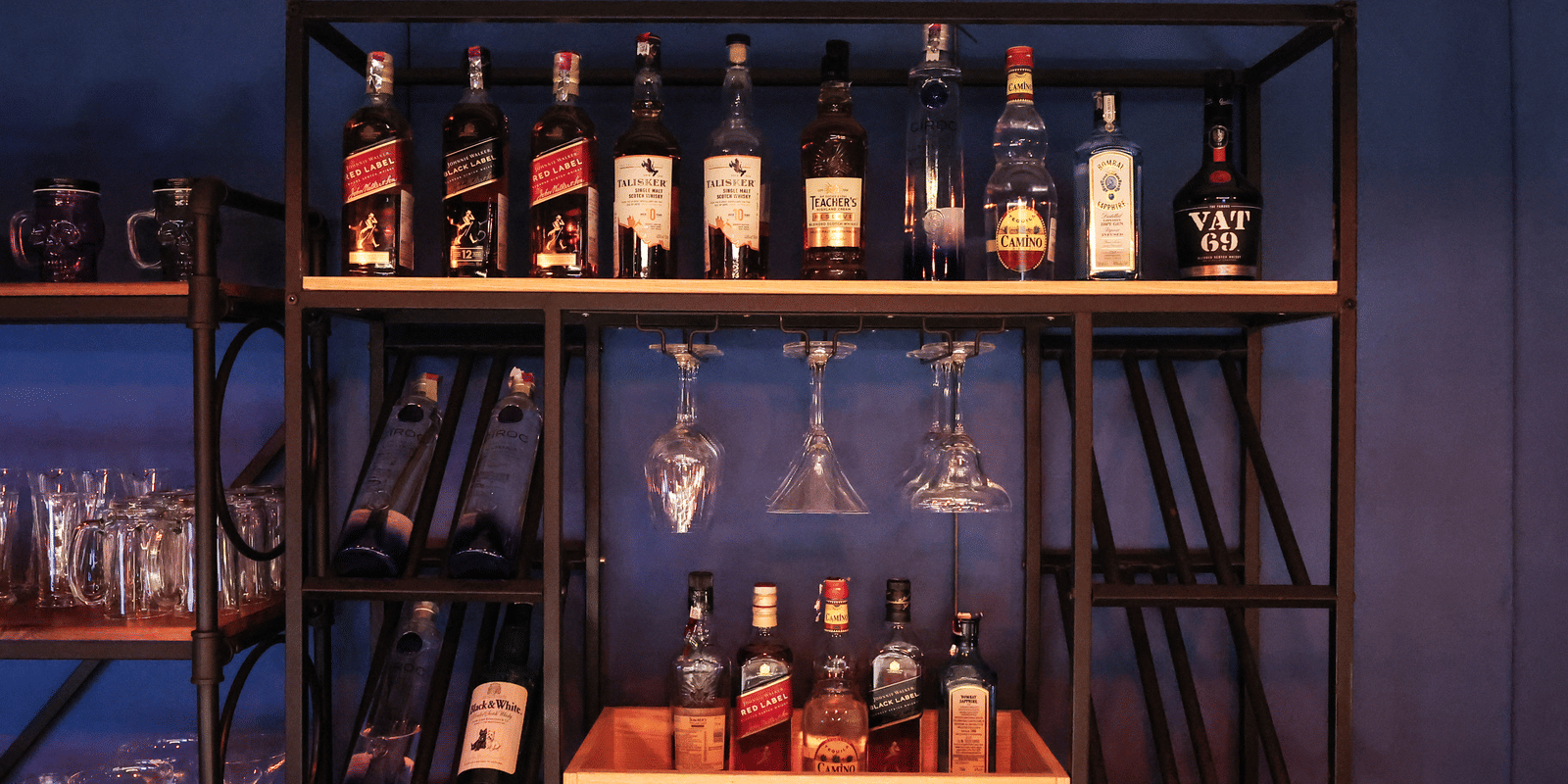 Close-up of the industrial-style black metal bar shelving with bottles of wine, spirits, and hanging glassware at Hotel Hukam's Lalit Mahal.