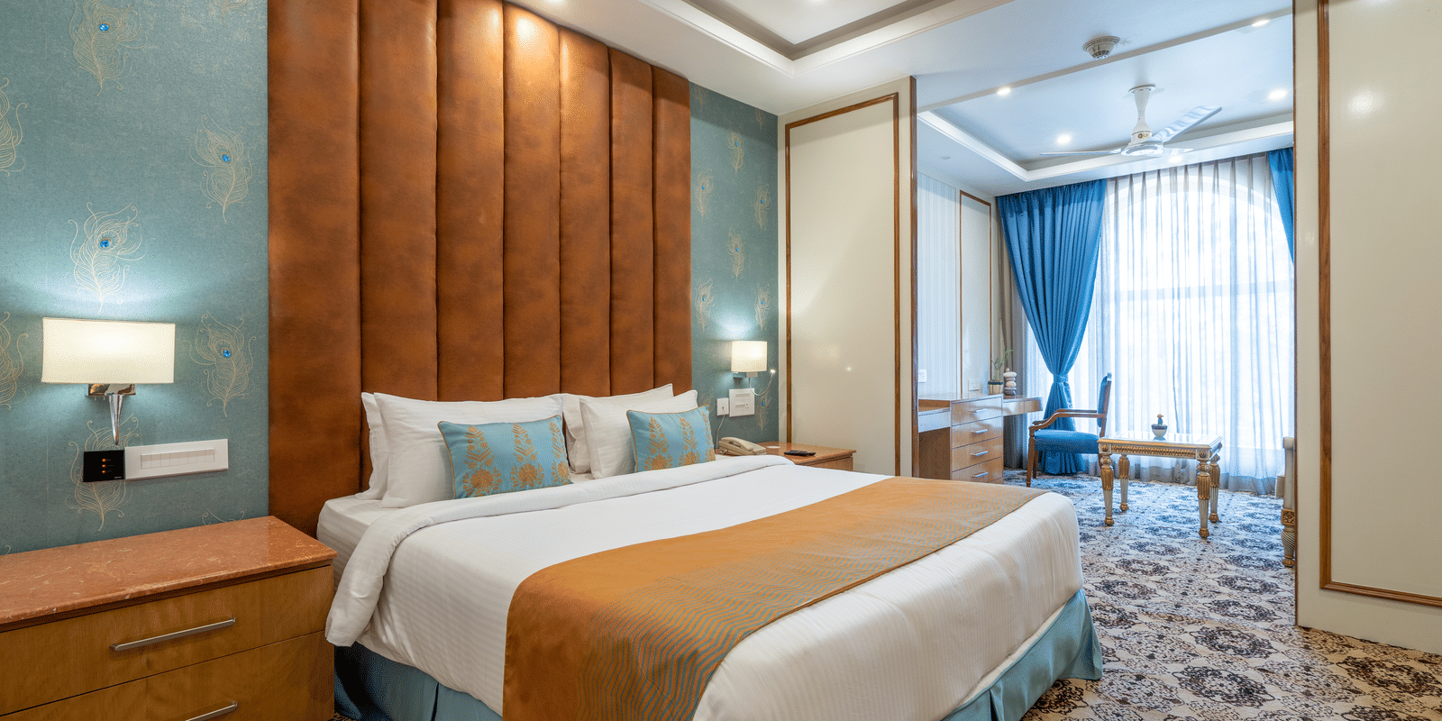 Wide shot of a contemporary hotel room with a spacious bed, nightstands, and a teal and terracotta colour scheme at Hotel Hukam's Lalit Mahal.