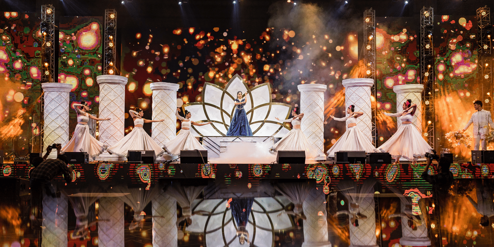 A dark stage background with glowing, ornate decor elements and intense warm stage lighting and sparkling effects at Hotel Hukam's Lalit Mahal.