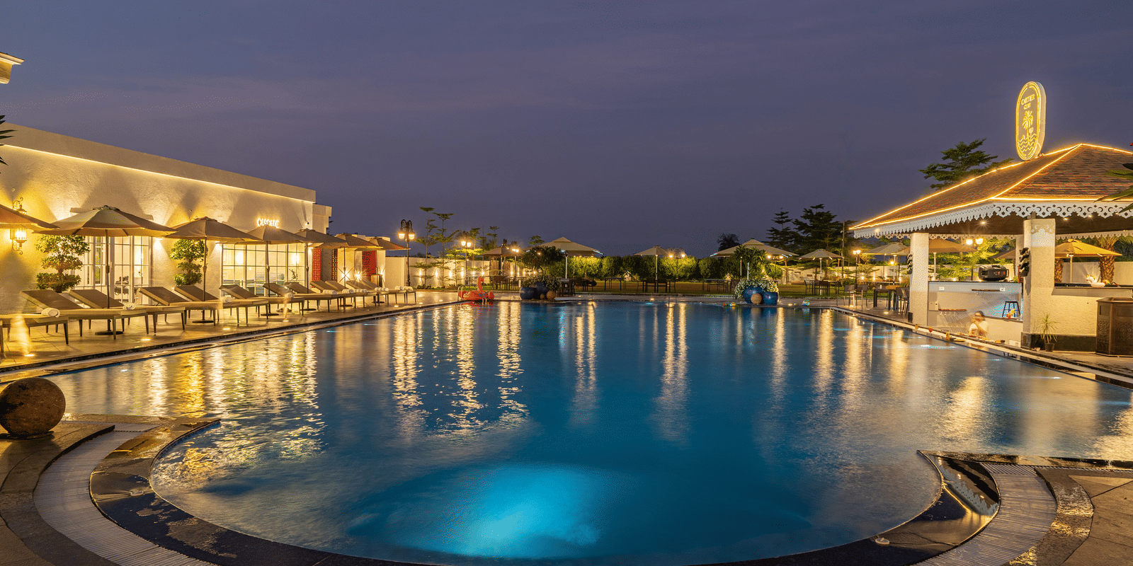 Outdoor swimming pool and surrounding buildings lit gently at dusk or early night, reflecting the sky and lights at Hotel Hukam's Lalit Mahal