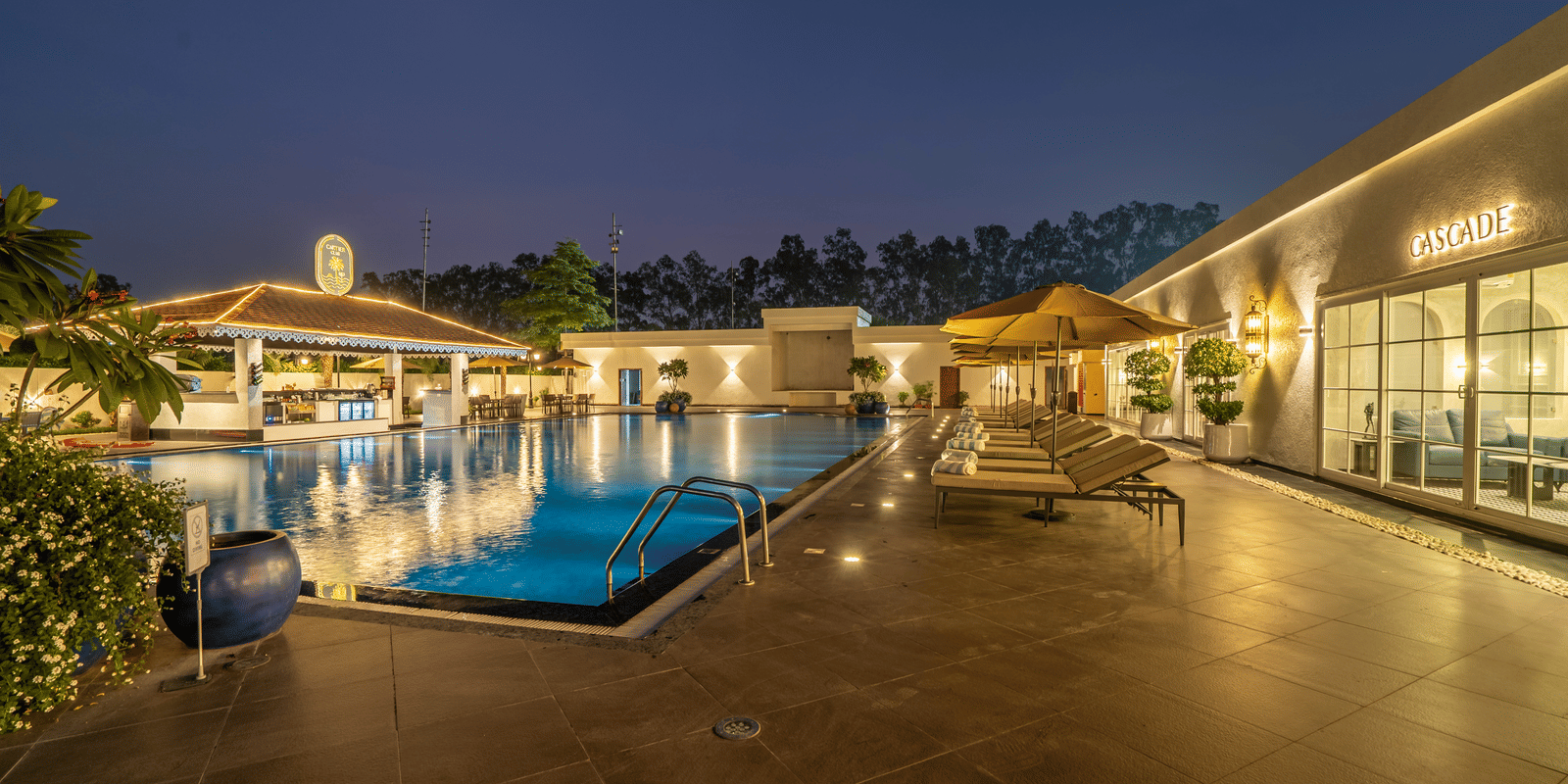Outdoor pool area at night with blue water and ambient warm lighting illuminating the surrounding deck and buildings at Hotel Hukam's Lalit Mahal.
