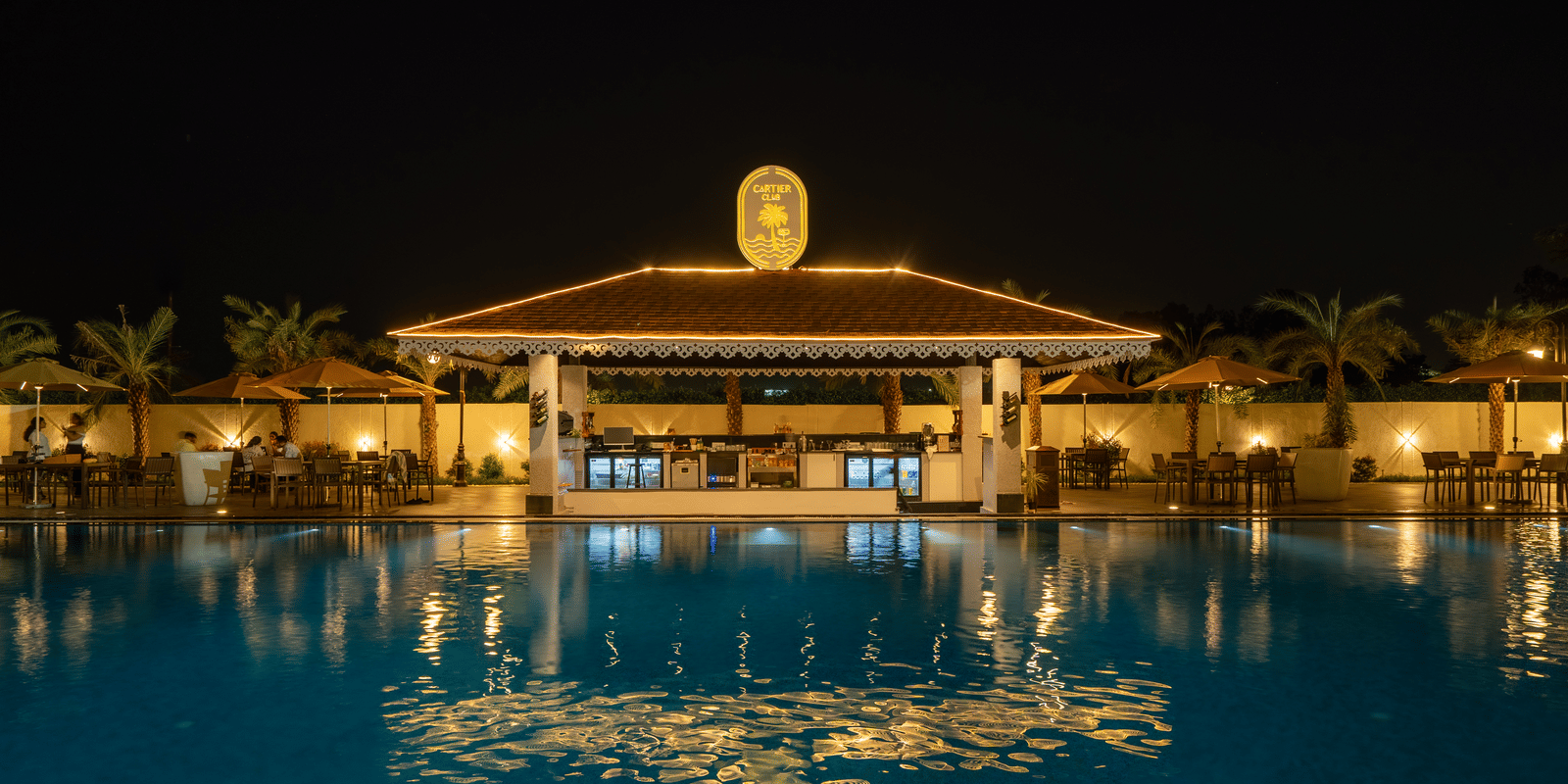 Poolside bar pavilion with its reflection visible in the calm, dark water of the swimming pool at night at Hotel Hukam's Lalit Mahal.