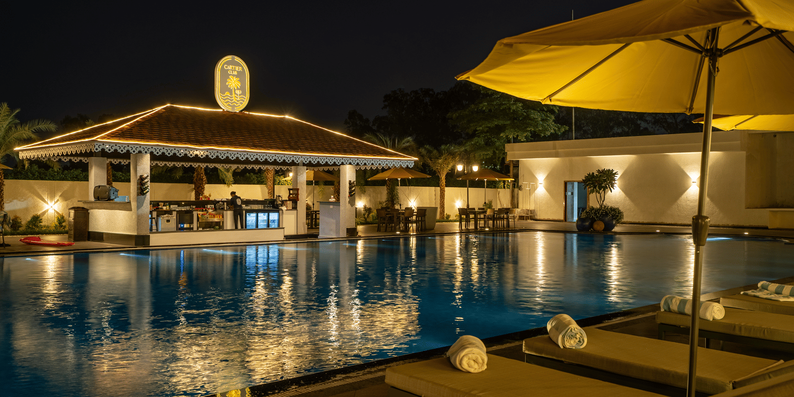 Evening view of the swim-up bar area next to the pool, featuring seating and ambient lighting under an umbrella at Hotel Hukam's Lalit Mahal.