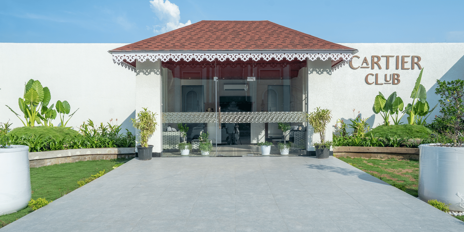 Exterior of the 'Cartier Club' building, a white structure with a red roof, fronted by a paved walkway and green lawn at Hotel Hukam's Lalit Mahal.