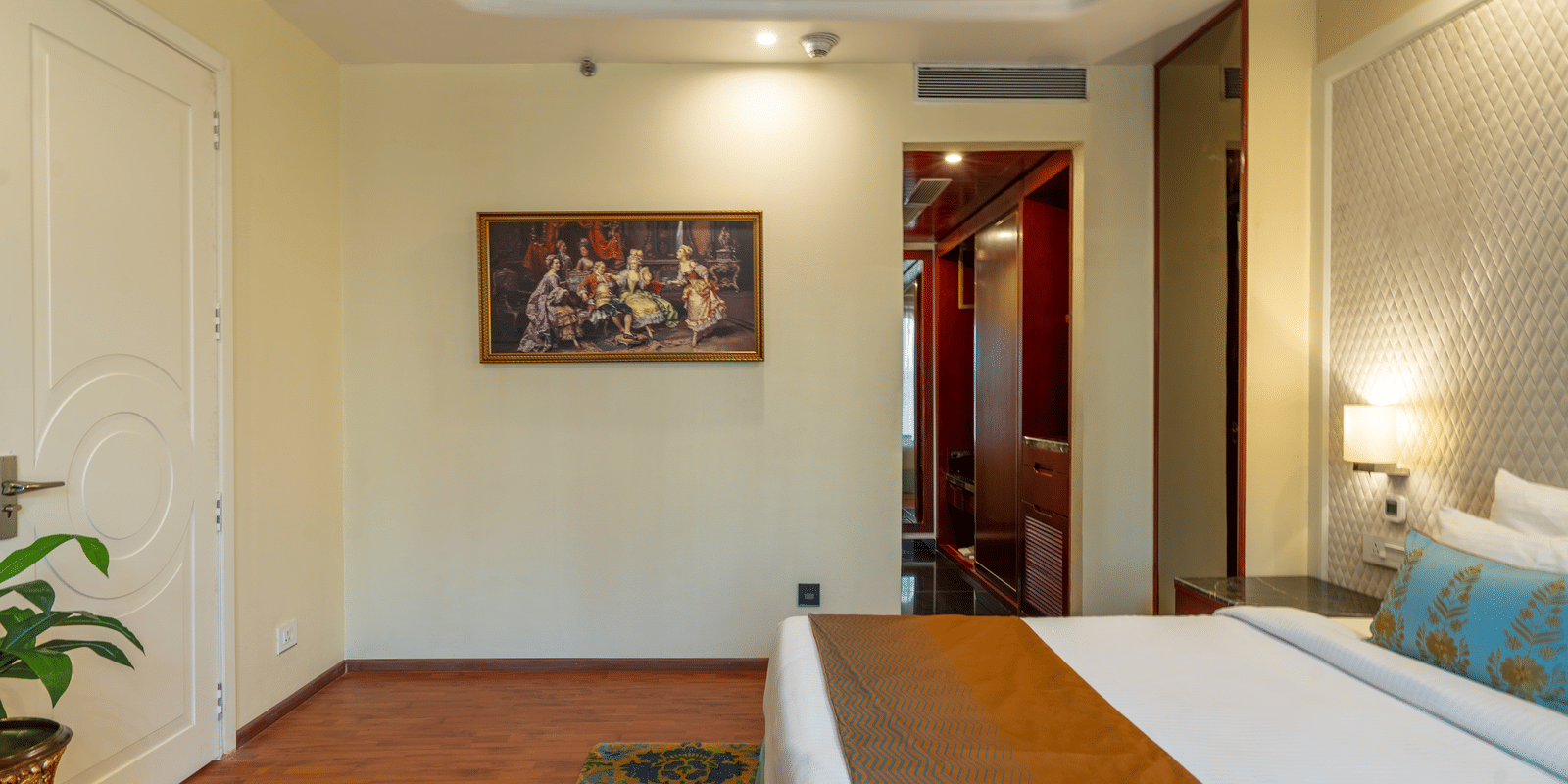Spacious hotel room with a large bed, picture frames on the wall, and detailed white wall panelling at Hotel Hukam's Lalit Mahal.