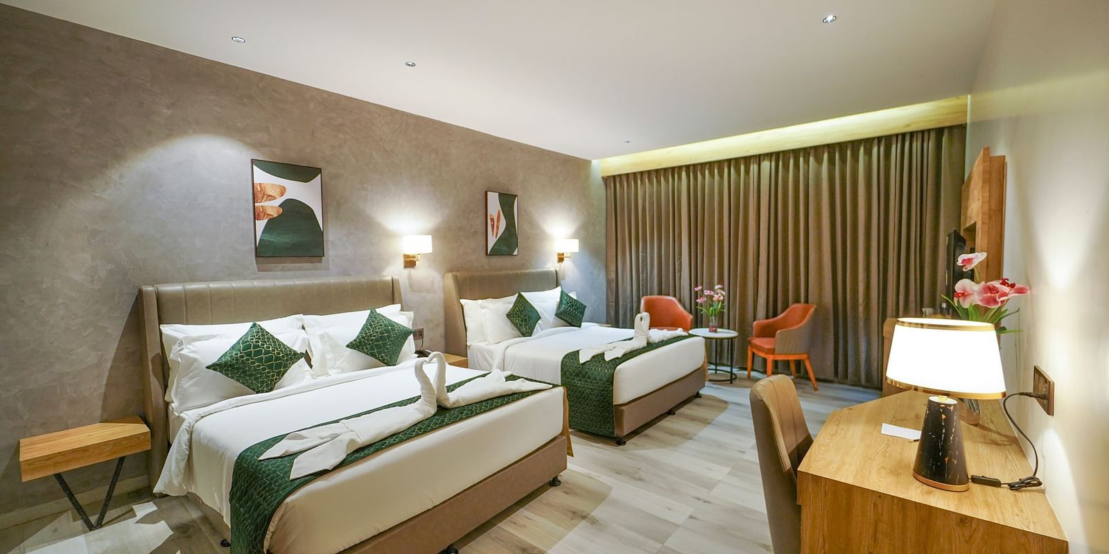 A hotel room offers two beds with decorative folded linens and pillows, a desk with a lamp and chair, and window curtains - Hotel Park Inn, Nellore.