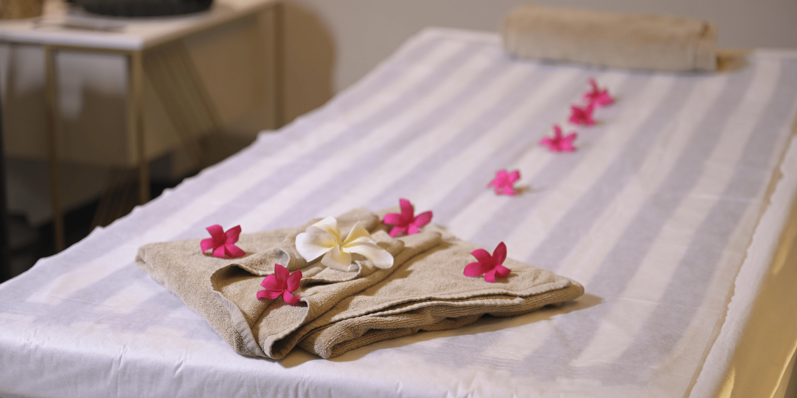 A massage bed decorated with folded towels and fresh pink flowers prepared for a therapy session at Hotel Sonar Bangla Mayapur.