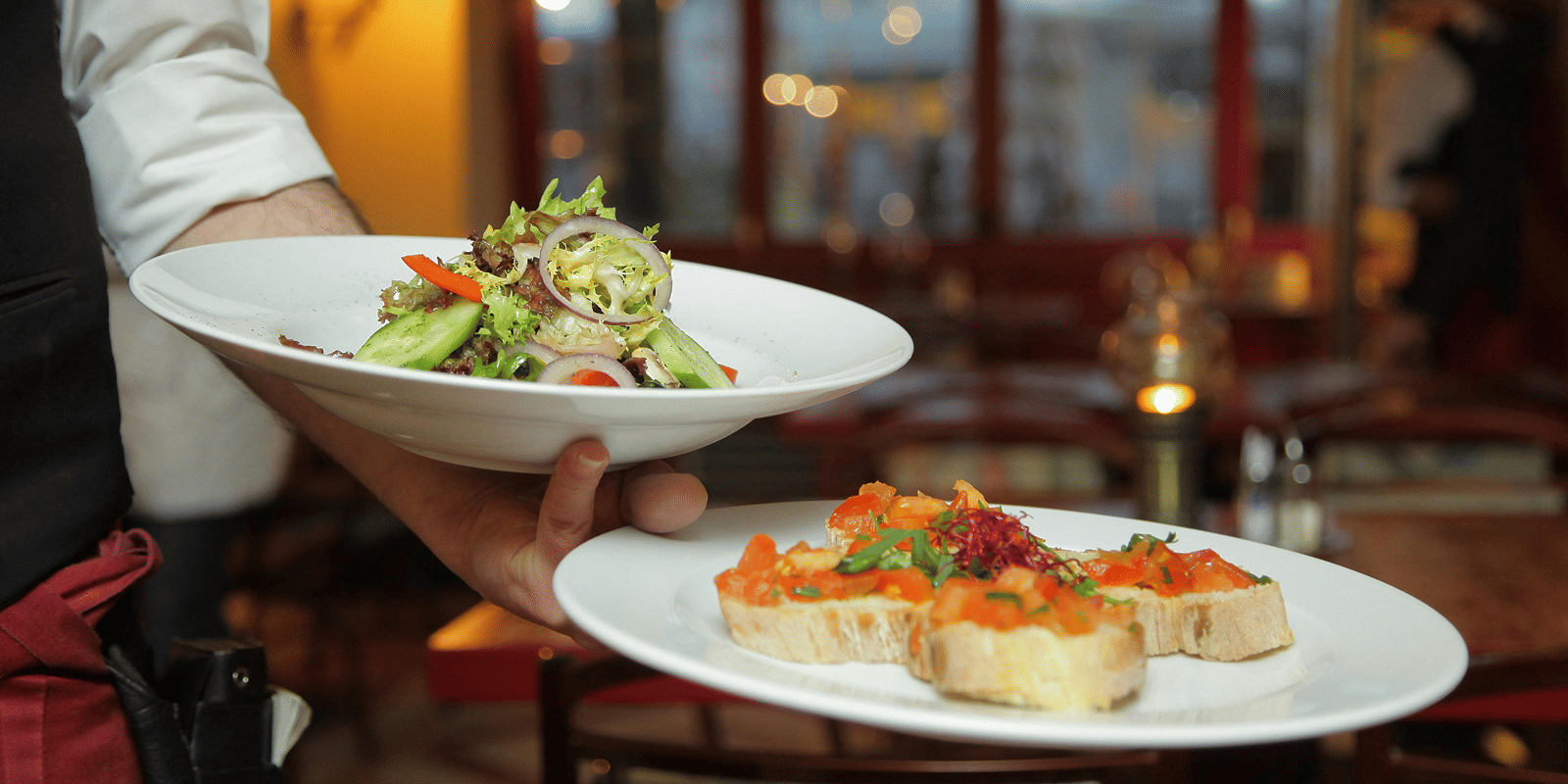a person in a restaurant holding two plates with delicious cuisines in it that are well plated