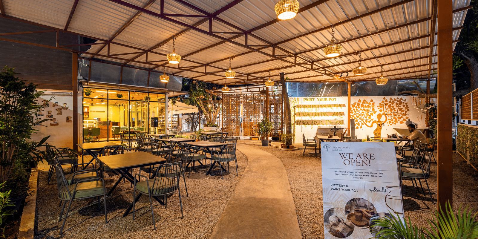 Claysutra Cafe And Restaurant at Kove Smart Stays seen during a darker time of the day, with ambient lighting, outdoor seating, and an overhead shed.