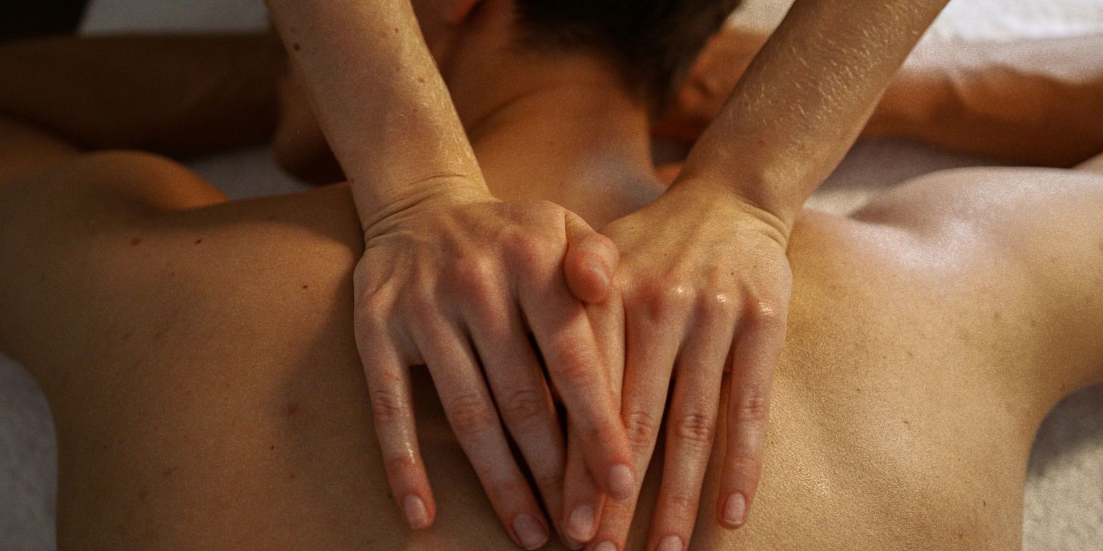 A massage therapist applying gentle pressure on a patient's back using both hands.