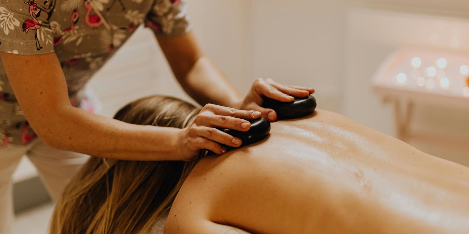 Therapist giving a hot stone back massage to a woman lying on a spa bed in a relaxing setting.