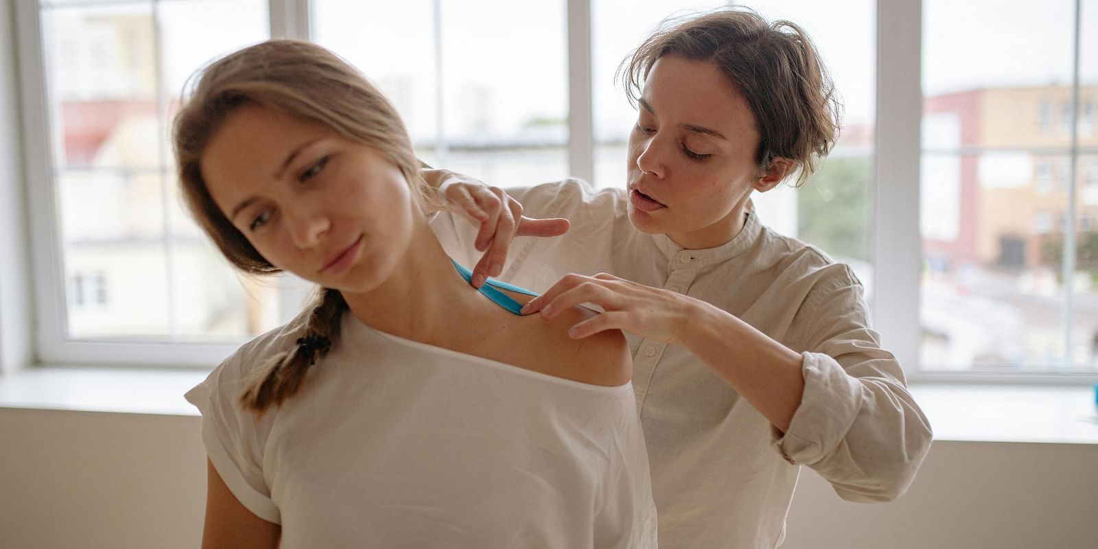 A therapist applying kinesiology tape to a patient's shoulder for support and pain relief.