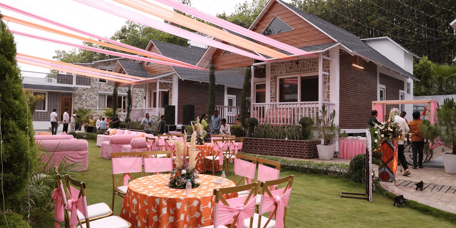 An outdoor event setup with pink and orange drapes, round tables, and chairs - Megha Resort & Villas, Dehradun