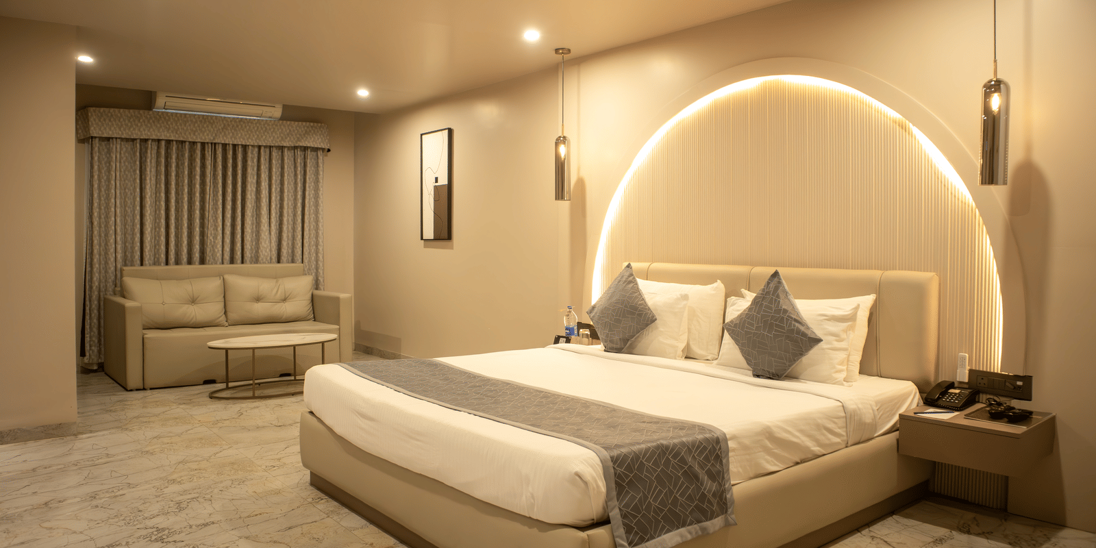 Wide view of bedroom at Papaya Tree Hotels Suite furnished with a double bed, a double-seating sofa, and and a bedside table. 