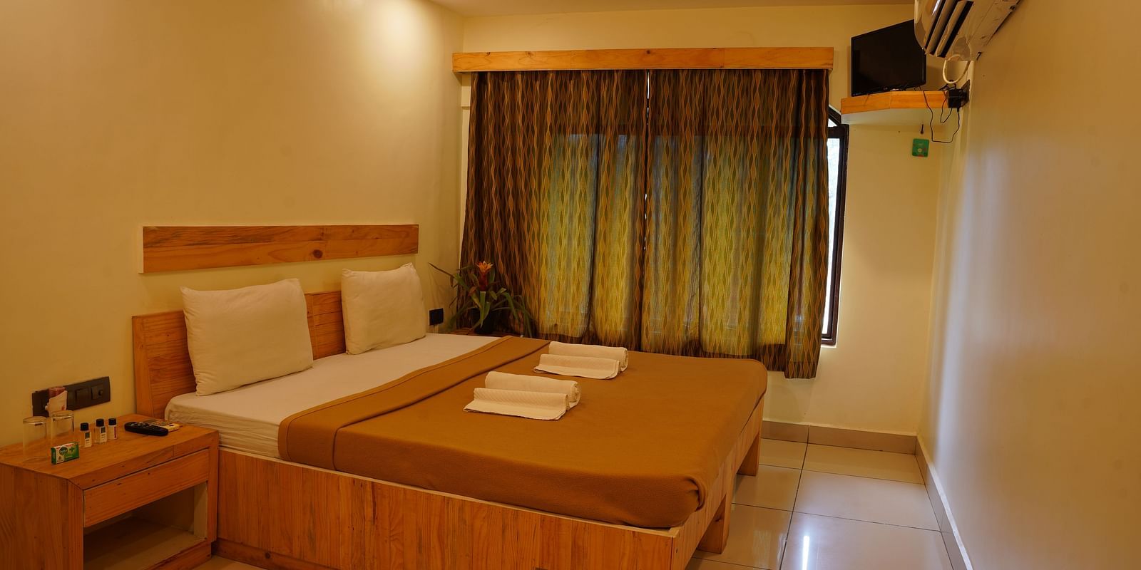 A side view of the room featuring a spacious bed, a bedside table, and a window covered with curtains at Riverside Inn.