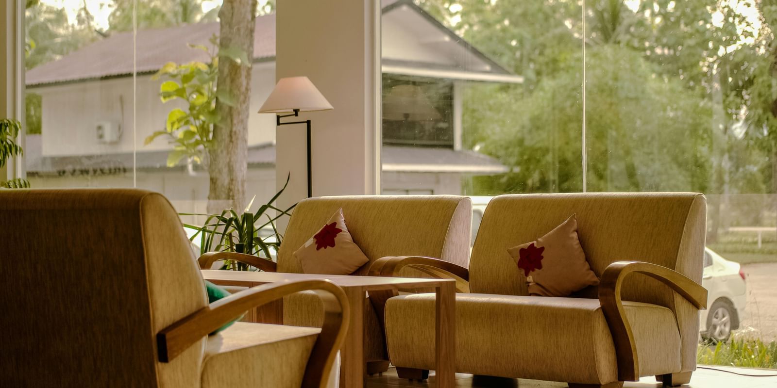 Comfortable seating area with beige armchairs, a small table, and decorative pillows near large windows overlooking greenery and buildings.