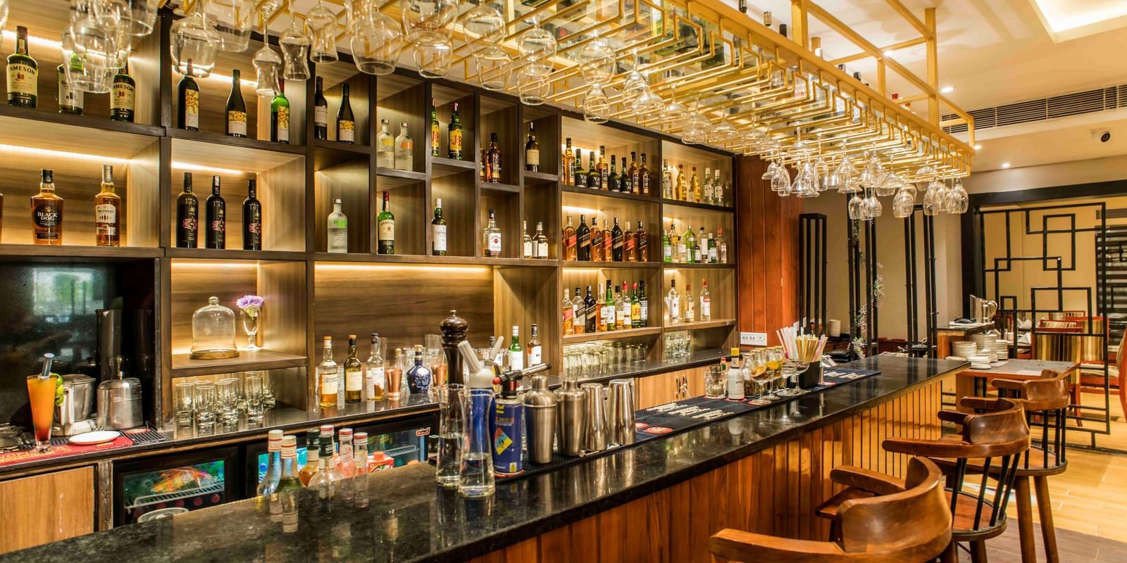 Well-stocked hotel bar with a dark countertop, multiple stools, and illuminated liquor bottles | The Citi Residenci Hotel Durgapur