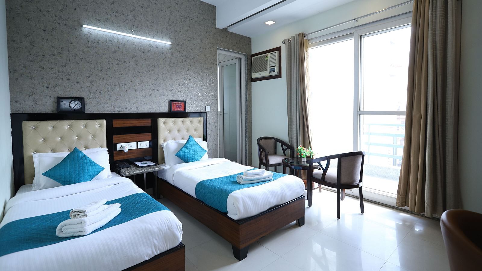 A comfortable room contains two single beds with blue accents, dark furniture, and a window with curtains - Asian Suites Cyber Park, Gurgaon