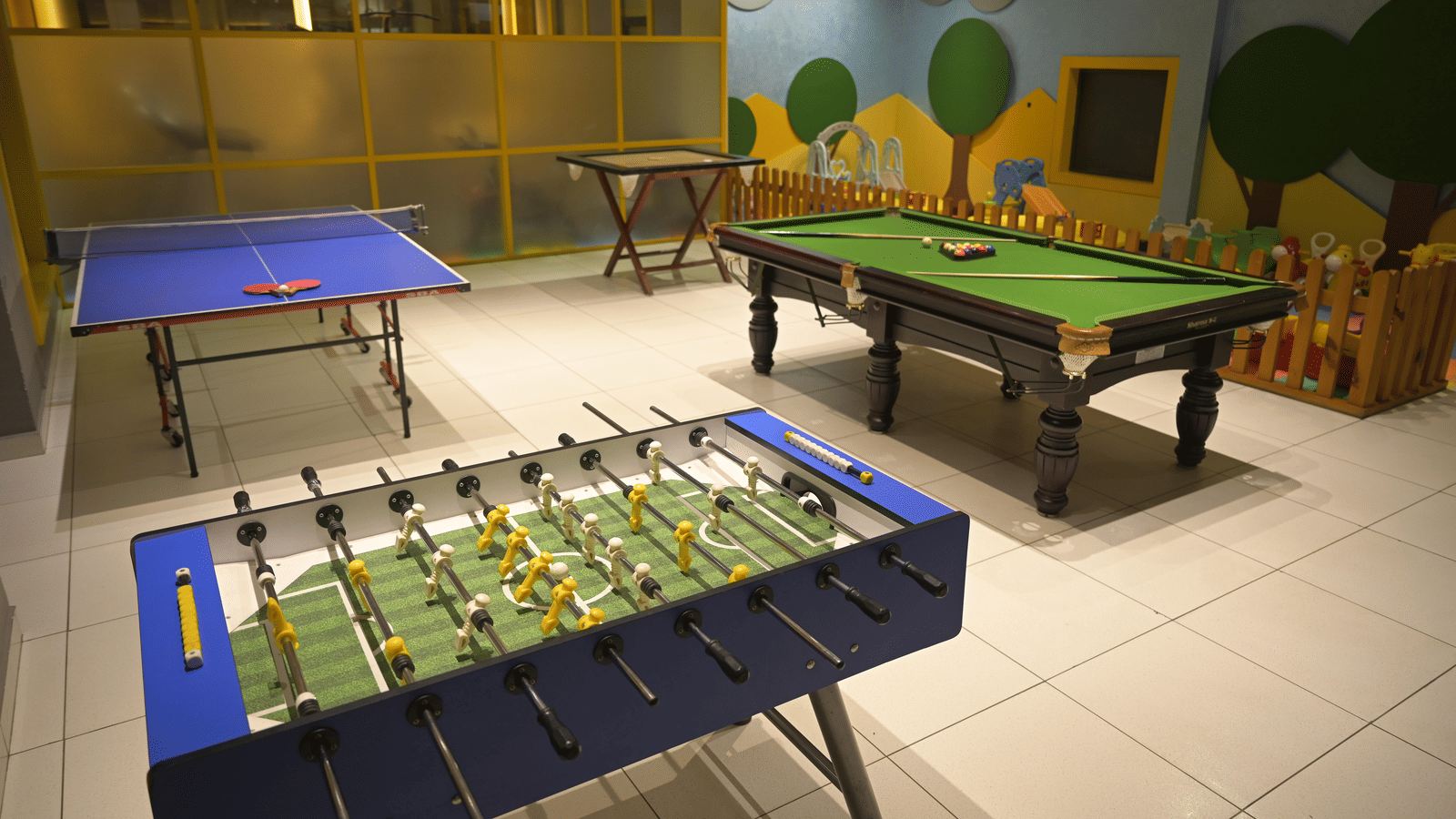 A bright indoor games room featuring a foosball table, a pool table, and a table tennis setup at Hotel Sonar Bangla Mayapur.
