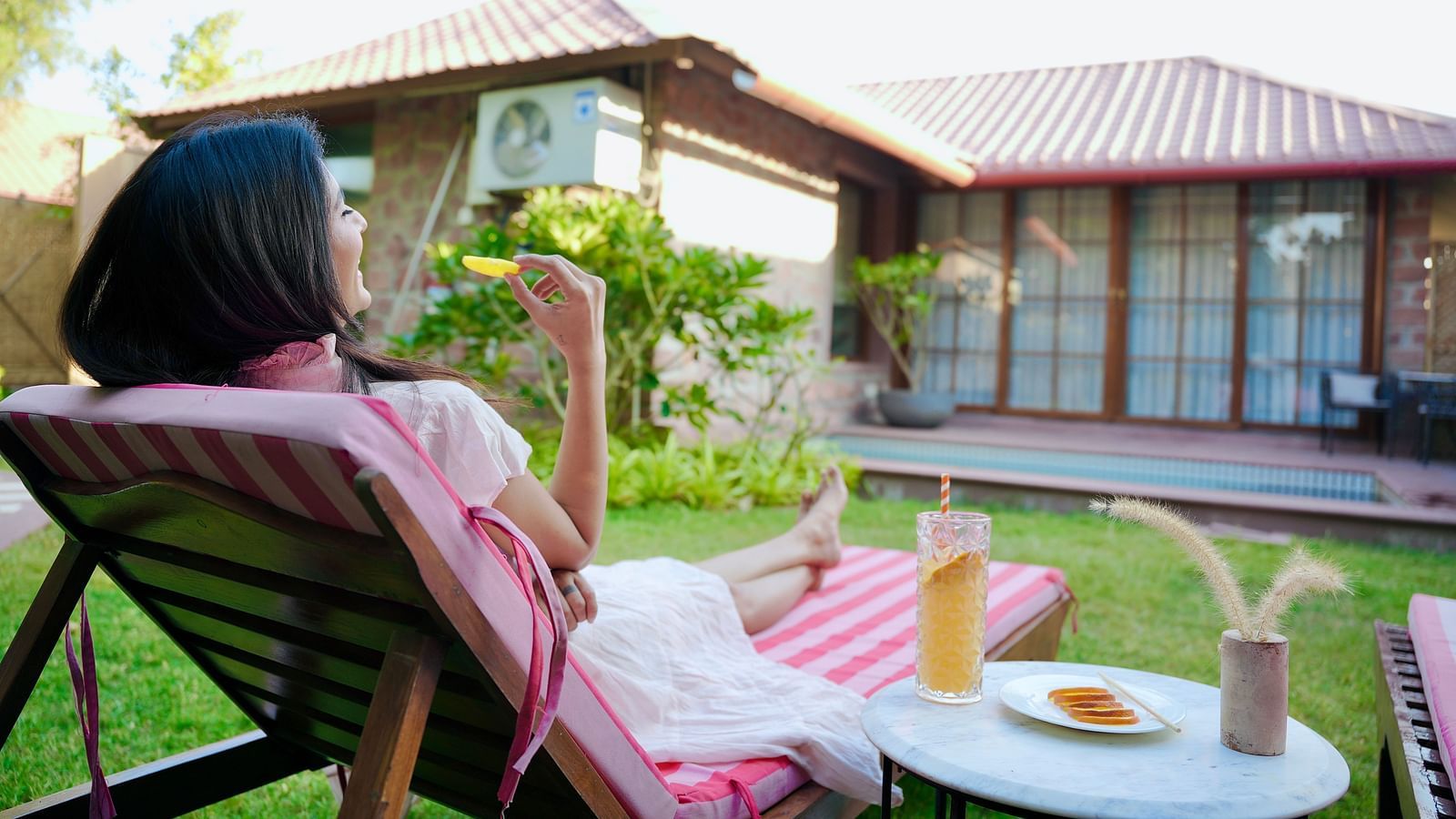 A woman seating on a lounge chair with drinks beside her at Surpura Bagh.
