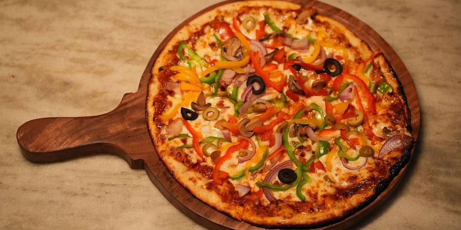 Loaded veggie pizza served on a wooden pizza plate at Rangamati Garden Resort.