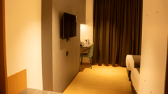 A bedroom with wall-mounted TV, desk, chair, 2 single beds, and closed curtains at Magnus Lxia Premier, Kalyani Nagar.