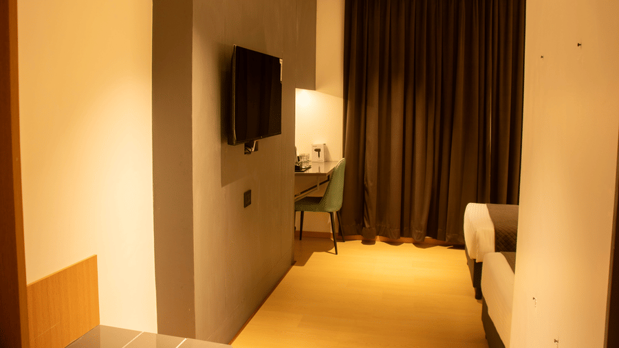 A bedroom with wall-mounted TV, desk, chair, 2 single beds, and closed curtains at Magnus Lxia Premier, Kalyani Nagar.