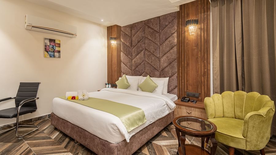 Image of Deluxe Room at DLS Grand Luxotica, Dehradun featuring a plush bed with a sitting space next to it by the window 
