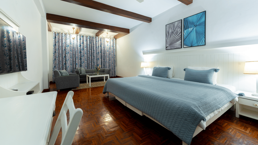 A large king size bed with blue linens, modern wall art, and exposed timber ceiling beams - Johnson Lodge & Spa, Manali