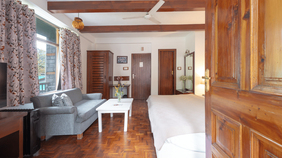 View of a luxury suite from the doorway showing the seating area, wooden finishes, and large windows - Johnson Lodge & Spa, Manali