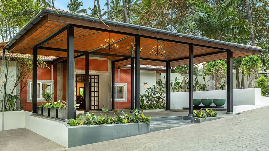 A building with a red brick exterior, a covered entrance with a terracotta tile roof, and palm trees in the background - Mango Hill Resort, Coimbatore