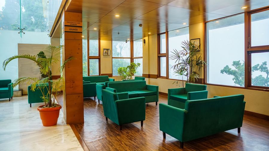 A lounge area with green armchairs and sofas arranged around small tables, with wooden accents and large windows at Orsino Spa Resort.