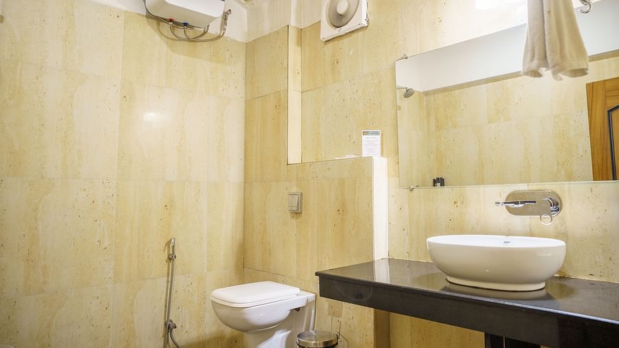A bathroom at Orsino Spa Resort with a white basin on a dark countertop, a toilet, and light-coloured tiled walls.