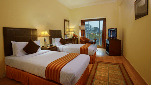 A bedroom featuring twin beds, a cabinet, bedside table with lamp, and a balcony attached