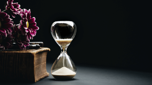 an hourglass that is counting down the time with pink flowers next to it