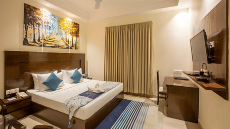 A stylish deluxe room with a large double bed, dark wood headboard, and a dedicated workspace desk — Eastlynn Resort, Rishikesh