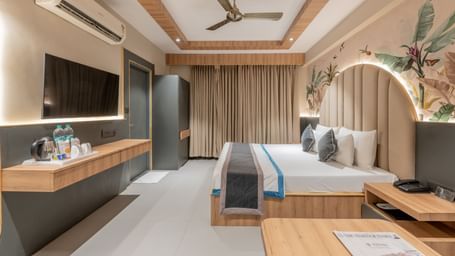 A wide view of the room featuring a king size bed, curtains, TV unit, mirror, and a wall mural at Hotel Highway King, Jaipur.