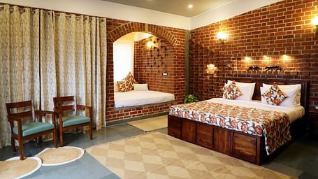 A bedroom at Tisya Farms, Gurgaon with a double bed, chairs, brick walls, curtains, and overhead lighting.