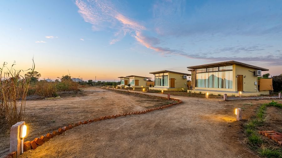 An image of cottages at Kurja Jawai with a huge lawn and some plants and an open sky behind 