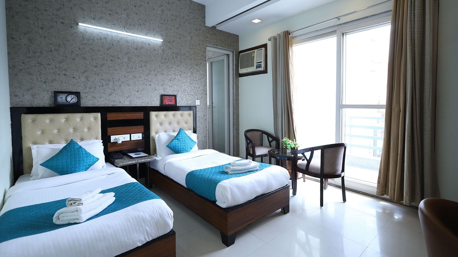 A comfortable room contains two single beds with blue accents, dark furniture, and a window with curtains - Asian Suites Cyber Park, Gurgaon