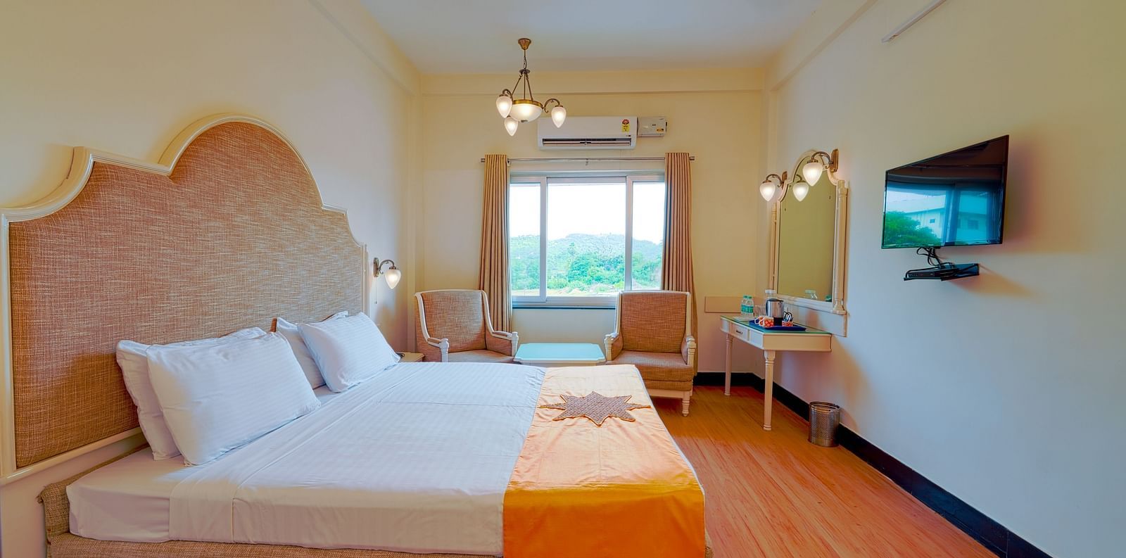 A well-appointed hotel room with a large bed, orange throw, wooden flooring, and a TV. - Greens Inn - Cozy Accommodations