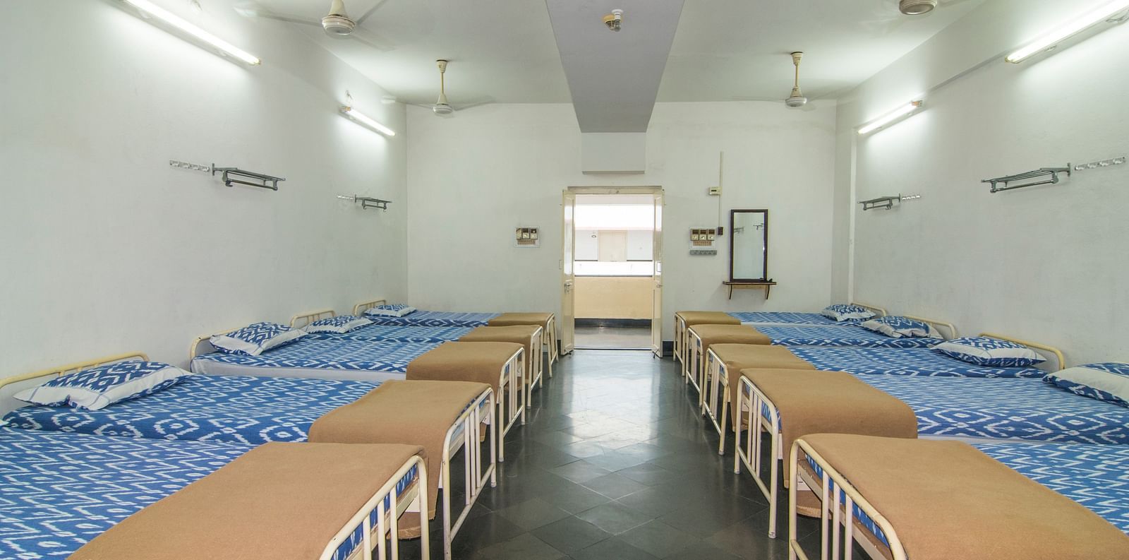 A full view of beds with bedding arranged in two rows in a room | Hotel Sahara