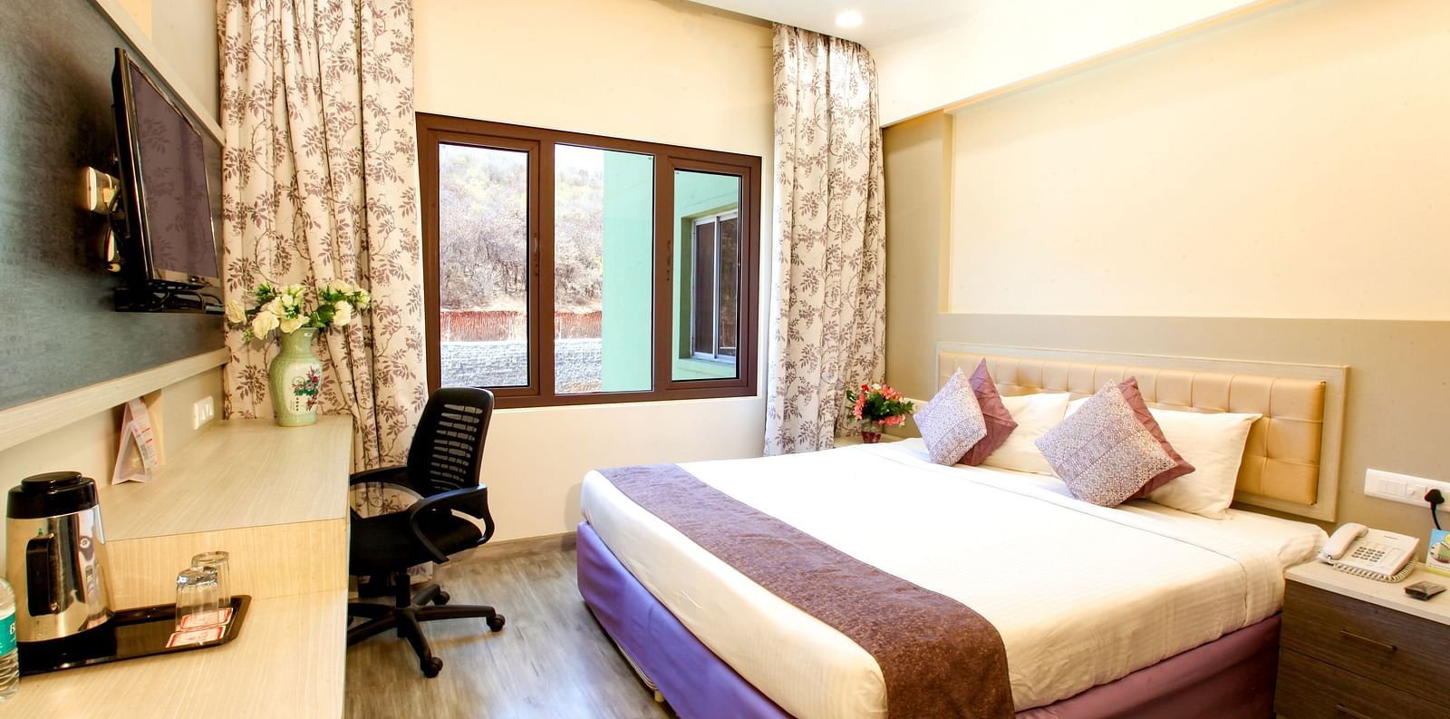 A modern hotel room with a plush king-sized bed and a view of the outdoors. - Tara, Comfort Hotel in Hyderabad - Ramoji Film City.