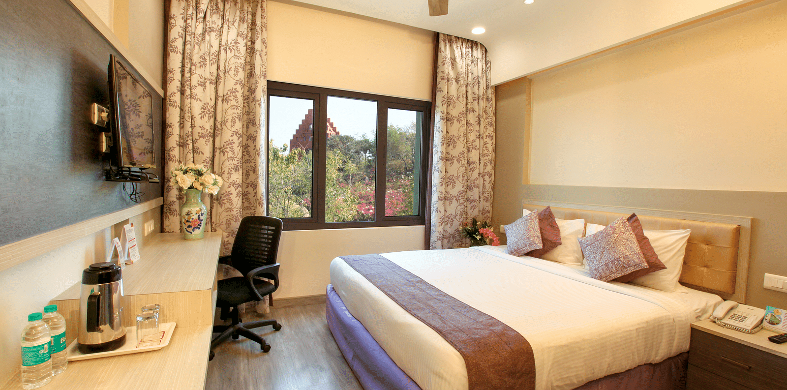 A spacious and elegantly decorated hotel room with a large window and a work area. - Tara, Comfort Hotel in Hyderabad - Ramoji Film City.