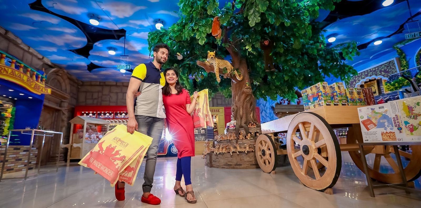 A couple standing in a vividly themed indoor amusement area designed to mimic an outdoor village market, complete with artificial trees and rustic carts at Ramoji Film City Hotels in Hyderabad 