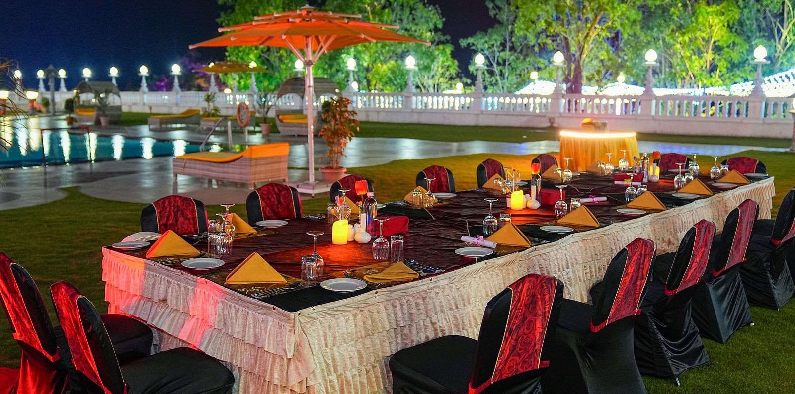 a set banquet table on a lawn with a swimming pool in the background at night - Ramoji Film City Hotels in Hyderabad 