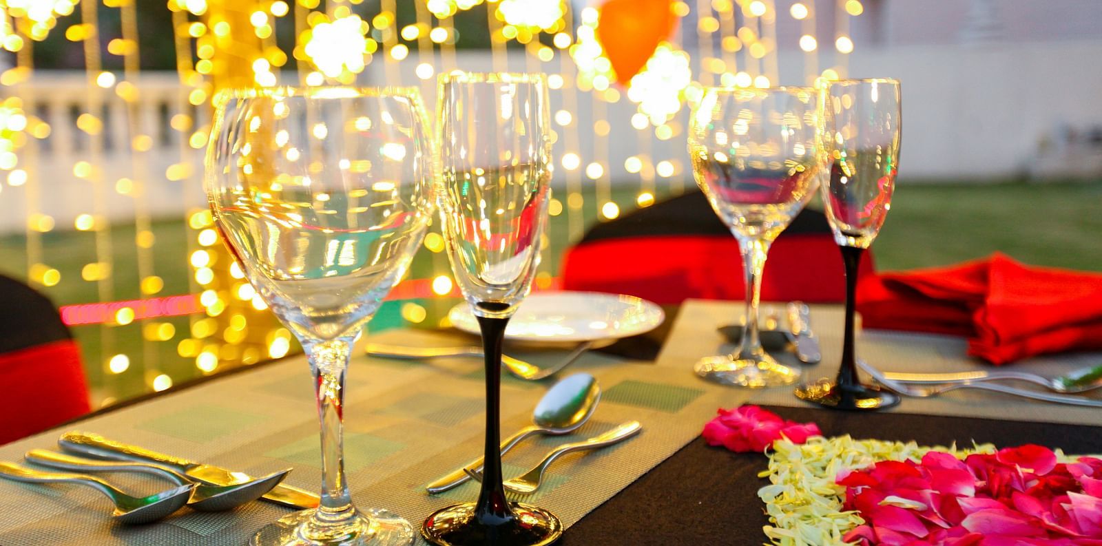 glasses set on a table with plates, cutlery and decoratations in the backdrop - Ramoji Film City Hotels in Hyderabad 
