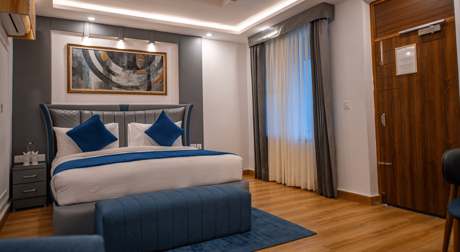 A Superior Room at The Tattva Devaprayag with a bed featuring blue blankets and two pillows, a sofa, and a framed painting on the wall.