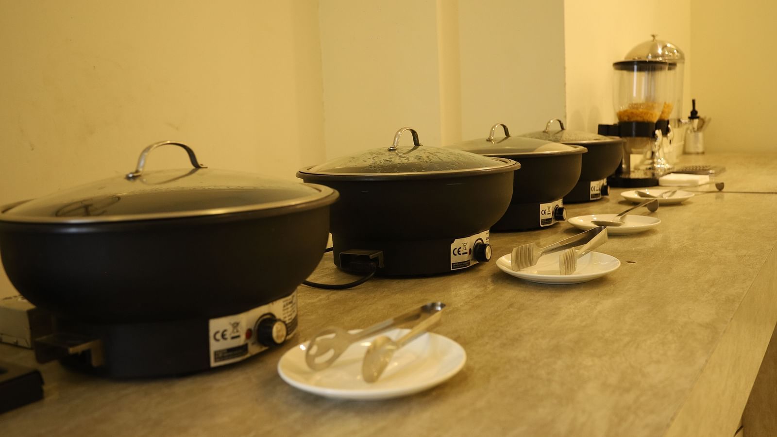 A close-up of a buffet setup shows large black serving dishes and various food items on a counter - Asian Suites Cyber Park, Gurgaon